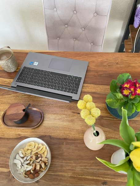 Arbeitsplatz mit Laptop, Pflanzen, einer Schale Nüsse und einer Vase mit Blumen.